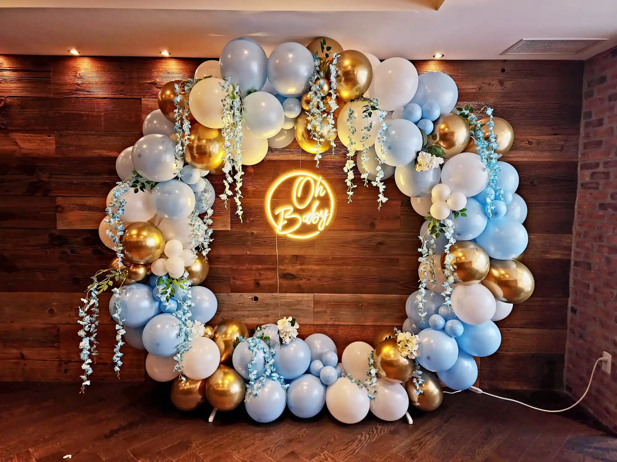 Blue and gold balloon garland arch with an 'Oh Baby' neon sign for an indoor baby shower