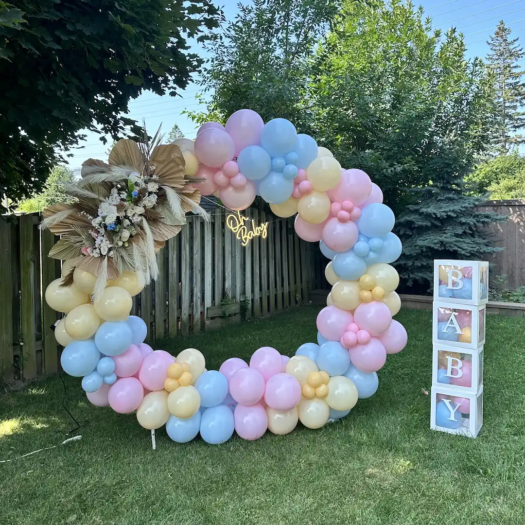 Pastel pink, blue and yellow balloon ring arch with an "Oh Baby" neon sign for an outdoor baby shower