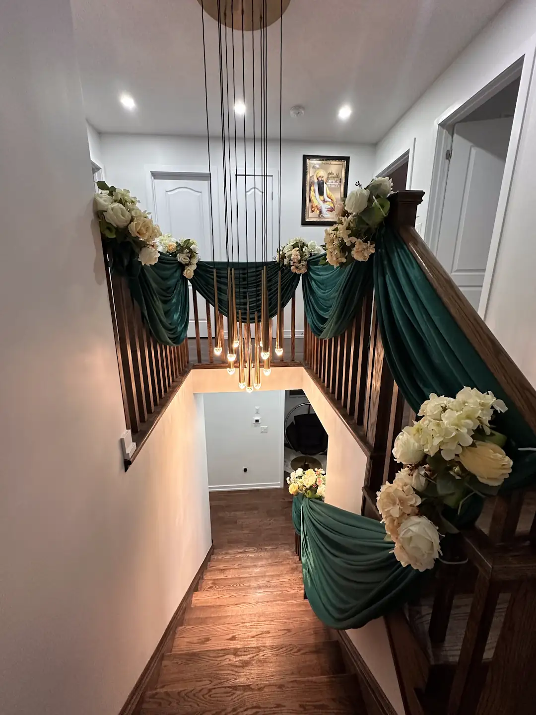 Staircase decorated with emerald green draping and white cream flower arrangements with a modern pendant chandelier